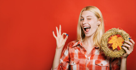 Happy winking girl with autumn wreath shows ok sign. Smiling woman with decorative autumn wreath....