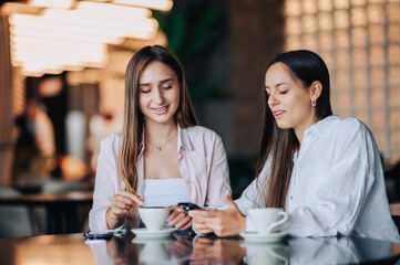 Two happy friends are sitting at the table in a cafe and chatting.