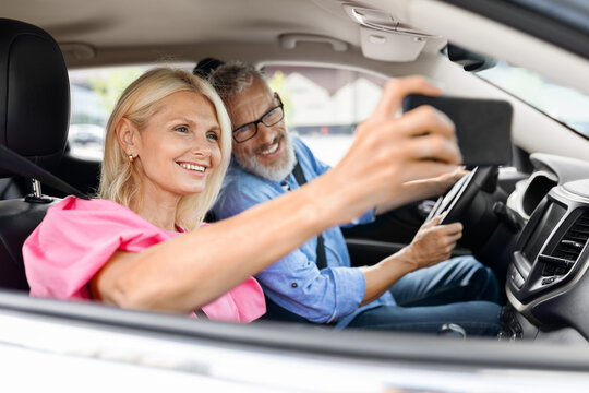 Happy elderly couple have car ride, taking selfie on phone
