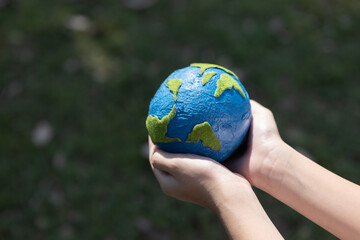 Young boy's hand holding planet Earth globe at natural park background as Earth day to save this planet with ESG principle and environment friendly energy for brighter future. Gyre