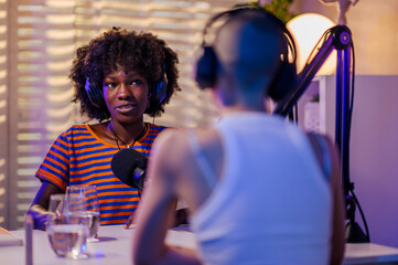 A multiracial journalist are interviewing a podcast guest in a home broadcasting studio.