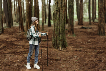 Positive young caucasian woman in jacket, hat with trekking sticks walk, enjoy adventure, free time