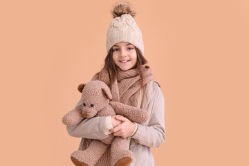 Cute little girl in winter clothes with toy bear on beige background