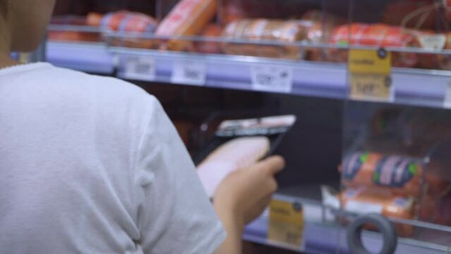A girl in a supermarket takes a product from the refrigerator. Sealed packaging of sliced meat. High quality FullHD footage