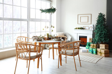 Interior of light living room with Christmas tree, fireplace and served dining table