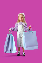 Cute little girl with shopping bags on purple background