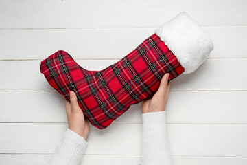 Female hands with Christmas sock on light wooden background, closeup