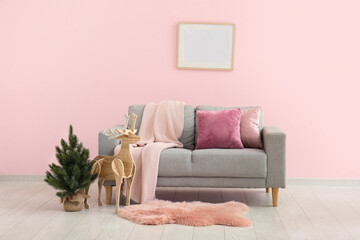 Interior of festive living room with grey sofa, small Christmas tree and wooden deer