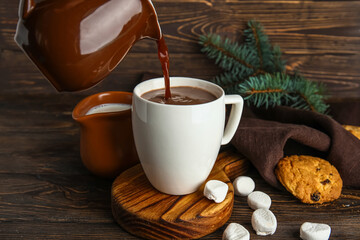 Pouring of tasty Christmas cocoa into cup on wooden background