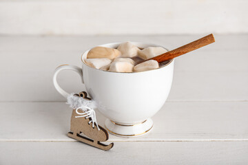 Cup of tasty Christmas cocoa with marshmallows, cinnamon and skates on white wooden background