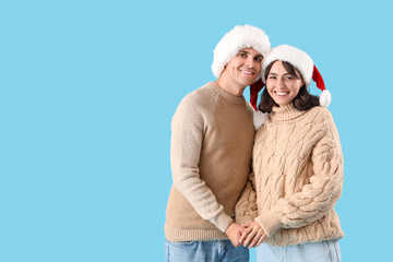 Happy young couple in Santa hats hugging on blue background