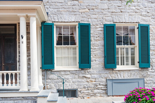 Two windows with green shutters and a door in the stone wall of the house.
