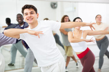 Smiling dark-haired young guy attending group choreography class, learning modern dynamic dances....