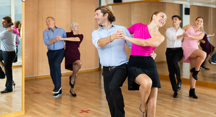 Dynamic middle-aged pair engaging in Latino dance in dance studio. Pairs training ballroom dance in hall