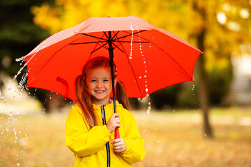 Happy child under summer rain. Funny girl have fun time while playing outdoors under autumn shower....
