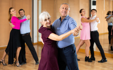 Dynamic aged pair engaging in ballroom dance in dance studio. Pairs training ballroom dance in hall