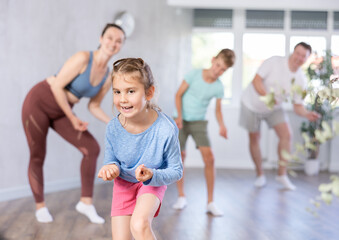 Sweet little girl training dance positions with her family members during workout session