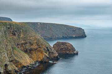 Santa Cruz Island, CA, USA - September 14, 2023: Yellow, brown and green colors in north facing shoreline cliffs. Light blue ocean and sky.