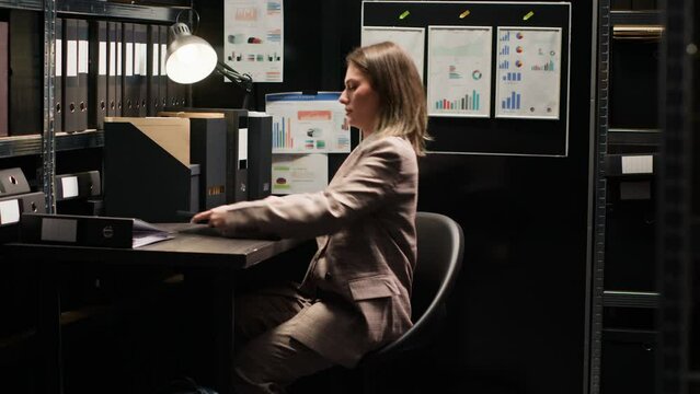 Diligent detective arrives and inspects evidence on personal computer to solve crime. Policewoman carrying bag enters office and places laptop on desk for reviewing records and analyzing clues.
