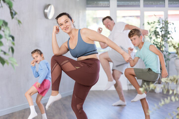 Obraz premium Joyful middle-aged woman training dance positions with her family members during workout session