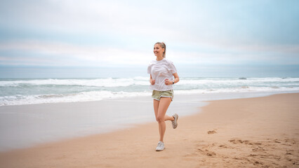 Woman jogging on beach. Sporty female jogging on sand beach, waves on background. Full body view...