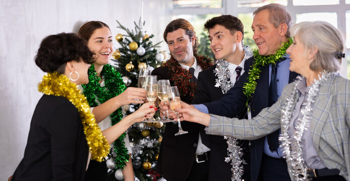 Excited colleagues of different ages with New Year tinsels clinking glasses of champagne during corporate party in office