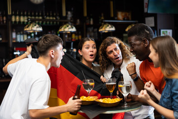 Diverse men and women supporting Germany sports team in pub together. Happy group of friends...