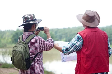 Tuinposter Back view of Asian woman and man travellers holds binocular and paper map to explore natural route for trekking beside the lake. Ecology study. Pastime activity, lifestyle. Explore environment   © Sanhanat