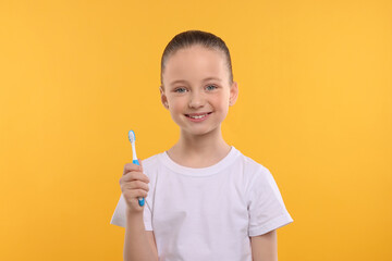 Happy girl holding toothbrush on yellow background