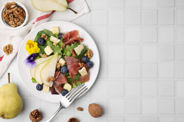 Tasty salad with brie cheese, prosciutto, walnuts and pear served on white tiled table, flat lay. Space for text