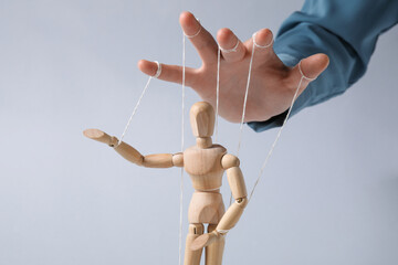 Woman pulling strings of puppet on light grey background, closeup