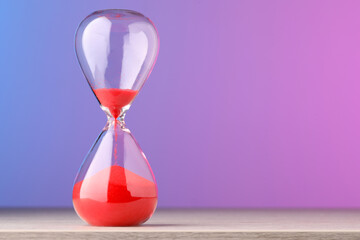 Hourglass with flowing red sand on table against color background, space for text