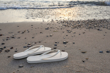 Fototapeta na wymiar Stylish white flip flops on sand near sea. Space for text