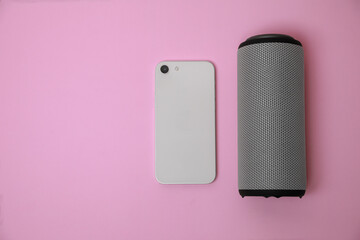 Portable bluetooth speaker and smartphone on pink background, flat lay with space for text. Audio...