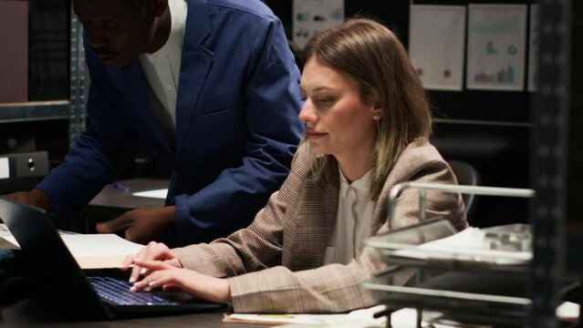 Multiethnic law enforcement agents conducting an investigation analyzing classified documents and evidence. Caucasian law officer uses laptop and discusses with policeman working towards justice.