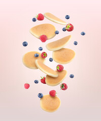 Many fresh pancakes and berries flying on pale pink background