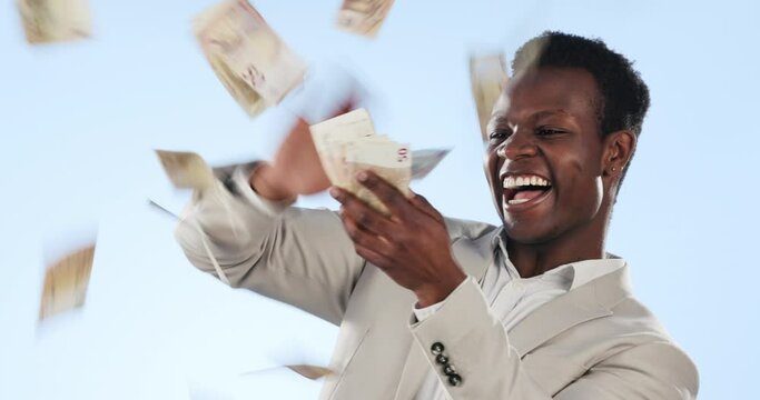 Happy black man, money rain and cash in financial freedom, winning or lottery against a studio background. African businessman blowing cash, dollar bills or paper notes in finance growth or profit