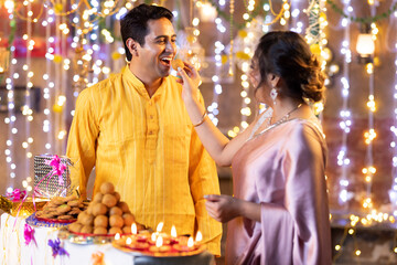 Indian smart couple eating sweet laddu on Diwali, selective focus
