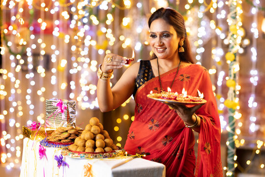 Smiling beautiful woman holding diyas while standing in illuminated house during Diwali festival