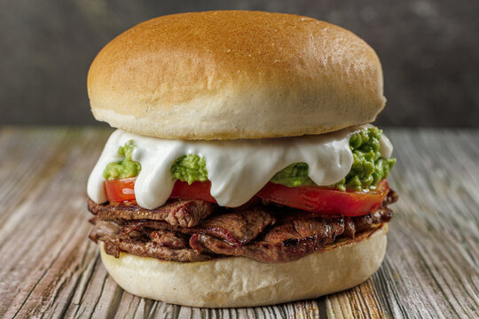 Churrasco italian sandwich popular in chile, round bread, beef, tomato and palta, mayonnaise, on wooden table. Typical Chilean food concept