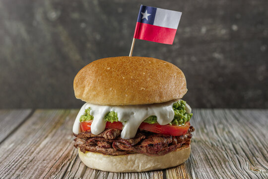 Churrasco italian sandwich popular in chile. with flag, round bread, beef, tomato and palta, mayonnaise, on wooden table. Typical Chilean food concept
