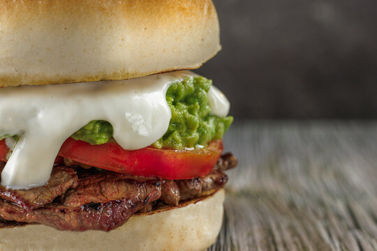 Churrasco italian sandwich popular in chile, round bread, beef, tomato and palta, mayonnaise, on wooden table. copy space. Typical Chilean food concept
