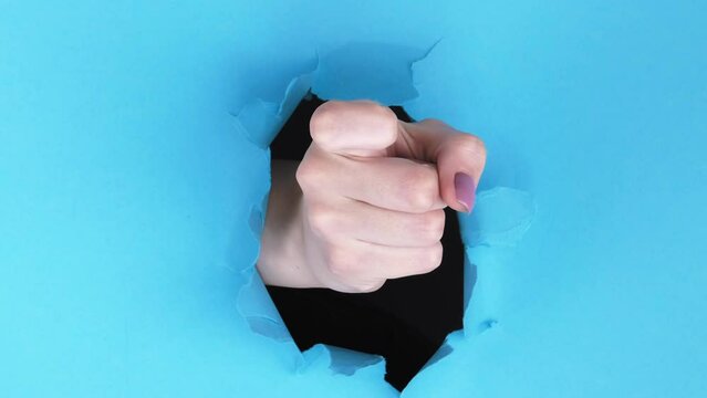 Vertical video. Come here. Follow gesture. Female hand inviting with finger inside breakthrough hole on blue ripped paper wall advertising background with empty space.