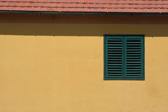 window with green shutters against yellow wall on house with space for text