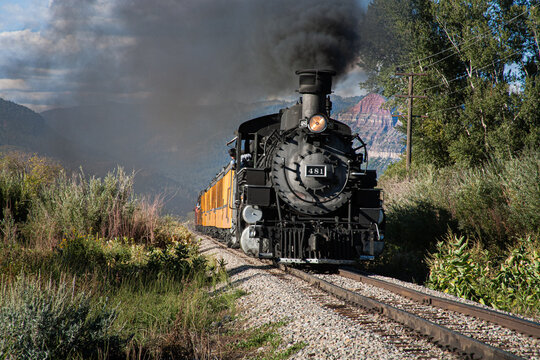 a steam engine train with smoke billowing from the smoke stack travels through the Colorado mountains an autumn day