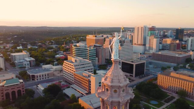 Austin Texas State Capital Building, Aerial Drone Shot Circling the Liberty Statue on Top with Views of The University of Texas at Austin and Downtown City Buildings Skyline at Sunset in 4K.