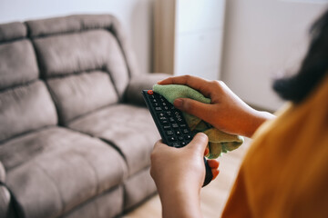 Young woman cleaning and disinfecting the television remote control with rag
