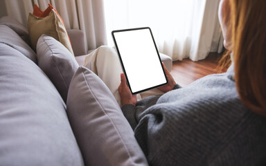 Mockup image of a woman holding digital tablet with blank desktop screen while lying on a sofa at...