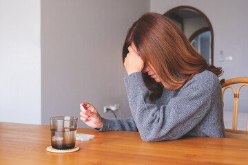 A sick woman holding pills and a glass of water on the table