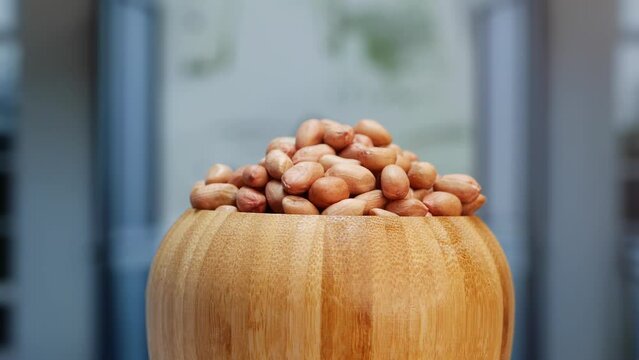 A bowl of peanuts on a wooden table. A wooden bowl filled with peanuts